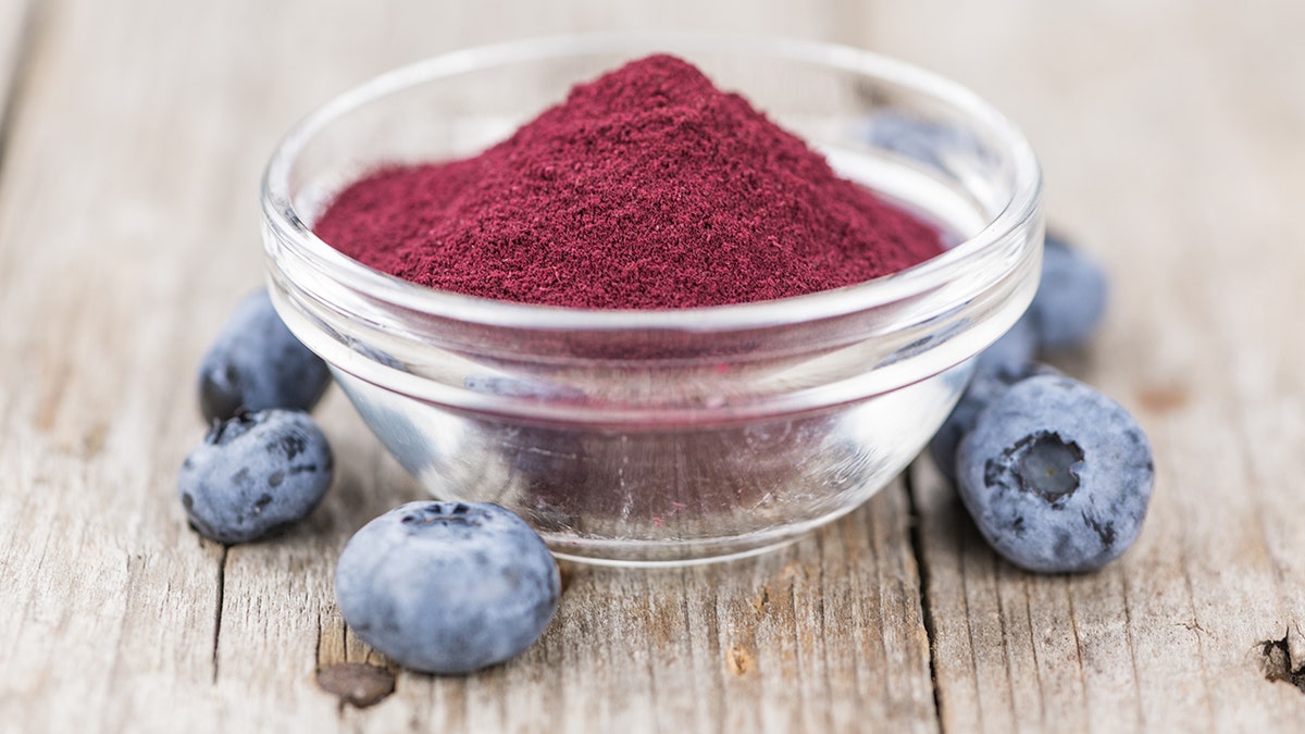 Blueberry powder seen in glass bowl on wooden table with scattered blueberries around it, representing new study on blueberries helping gut health, immunities and allergy relief.
