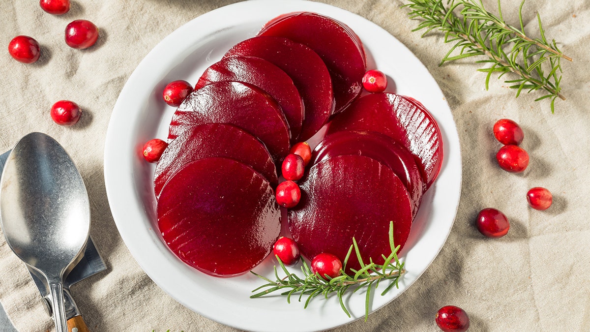 Canned cranberries are canned on a plate and surrounding holiday tables are surrounded by decor, including cranberries.