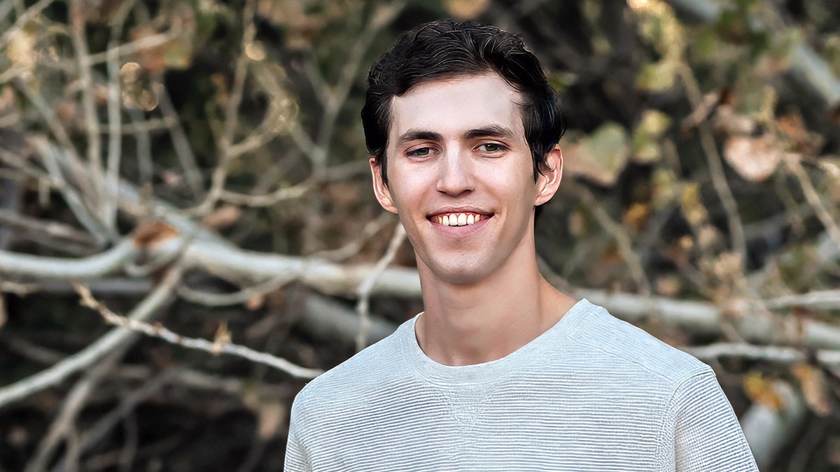 Tyler Robinson in a white shirt in front of some brush, smiling