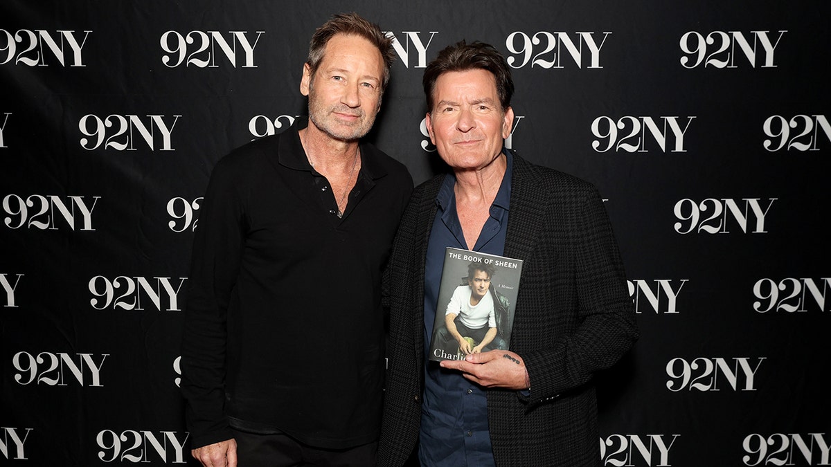 Charlie Sheen posing with David Duchovny while holding his book.