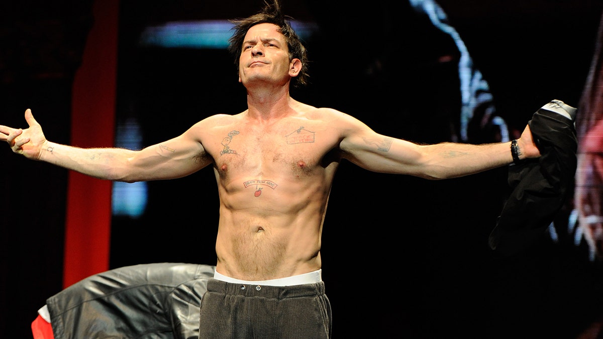 Charlie Sheen shirtless with his arms outstretched.