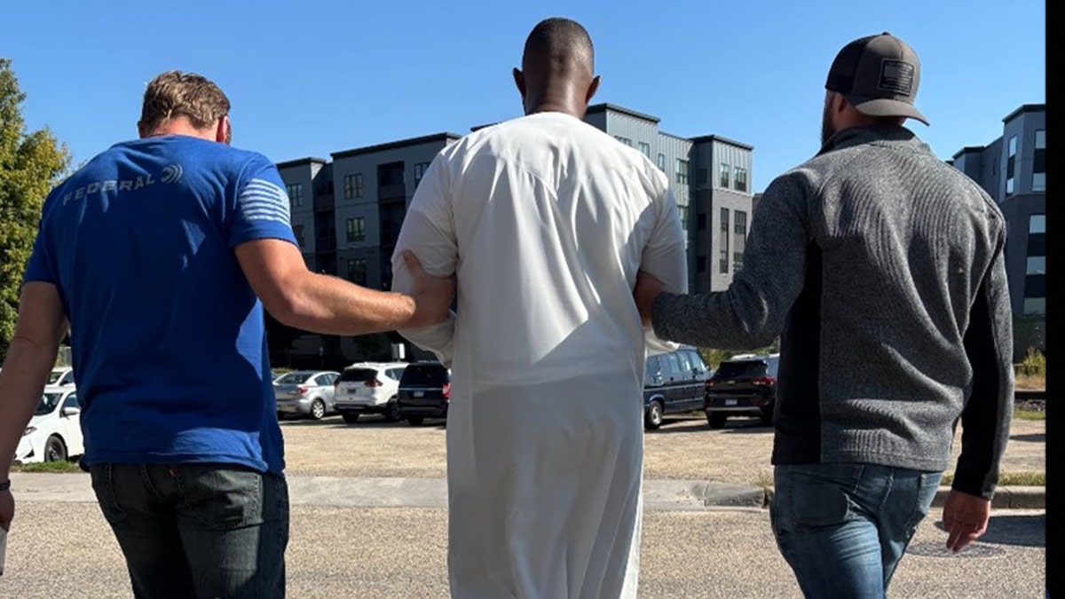 Oficiais do USCIS caminham ao longo de um migrante detido