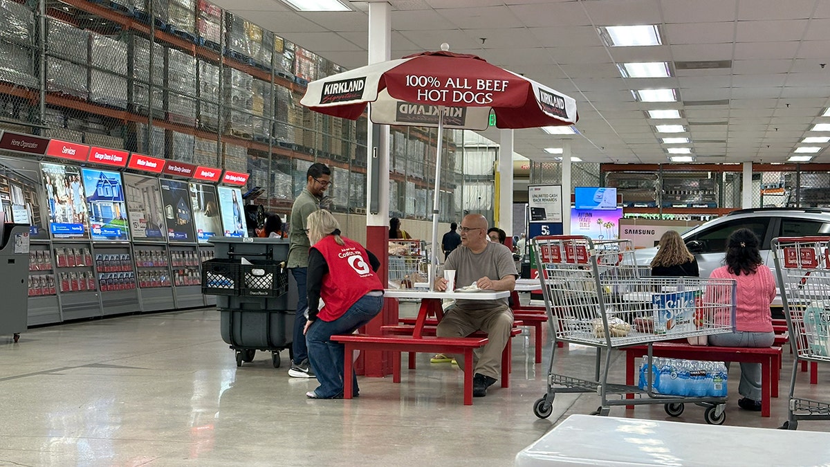 A Costco customer eats while talking to two employees.