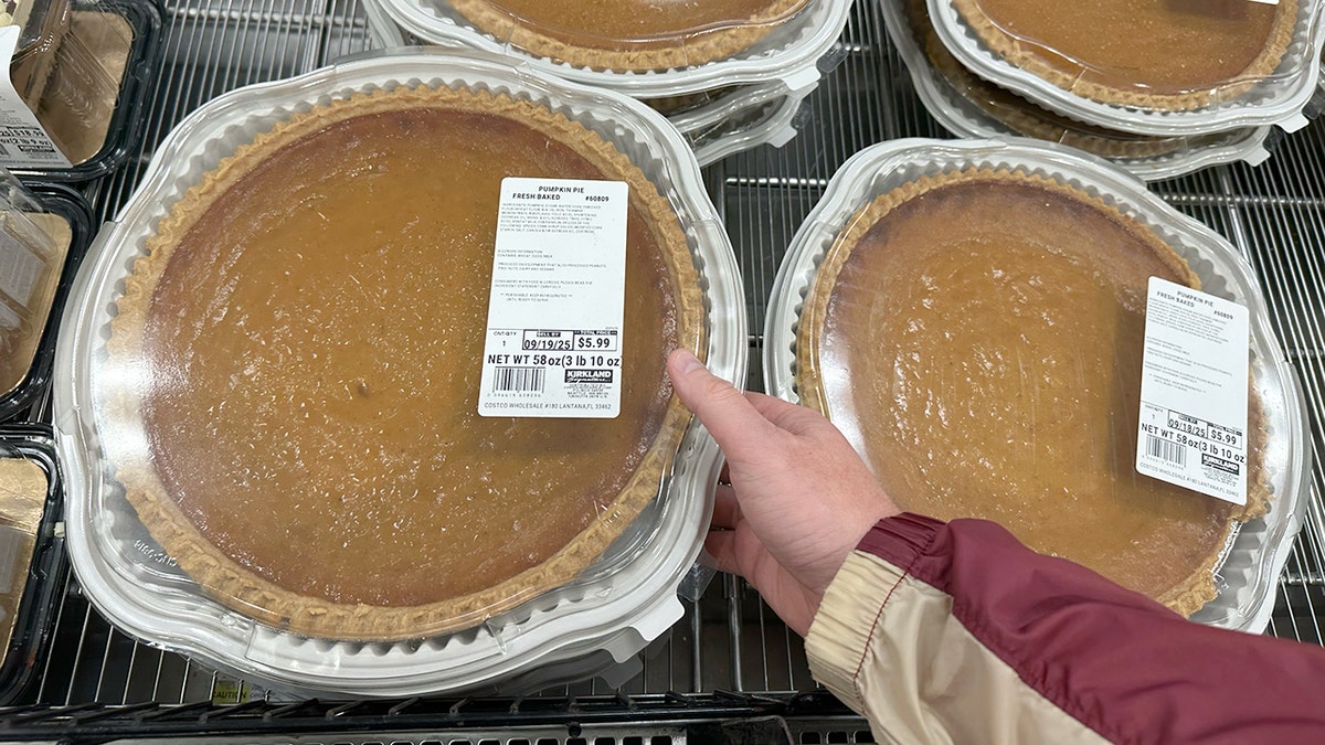 A hand picks up a giant Kirkland Signature pumpkin pie at Costco.