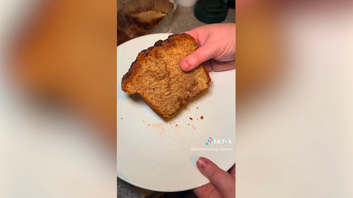 People hold a slice of Kirkland signature butter cinnamon sugar bread from Costco, showing cinnamon through the swirls of bread on a plate and loading in the background.