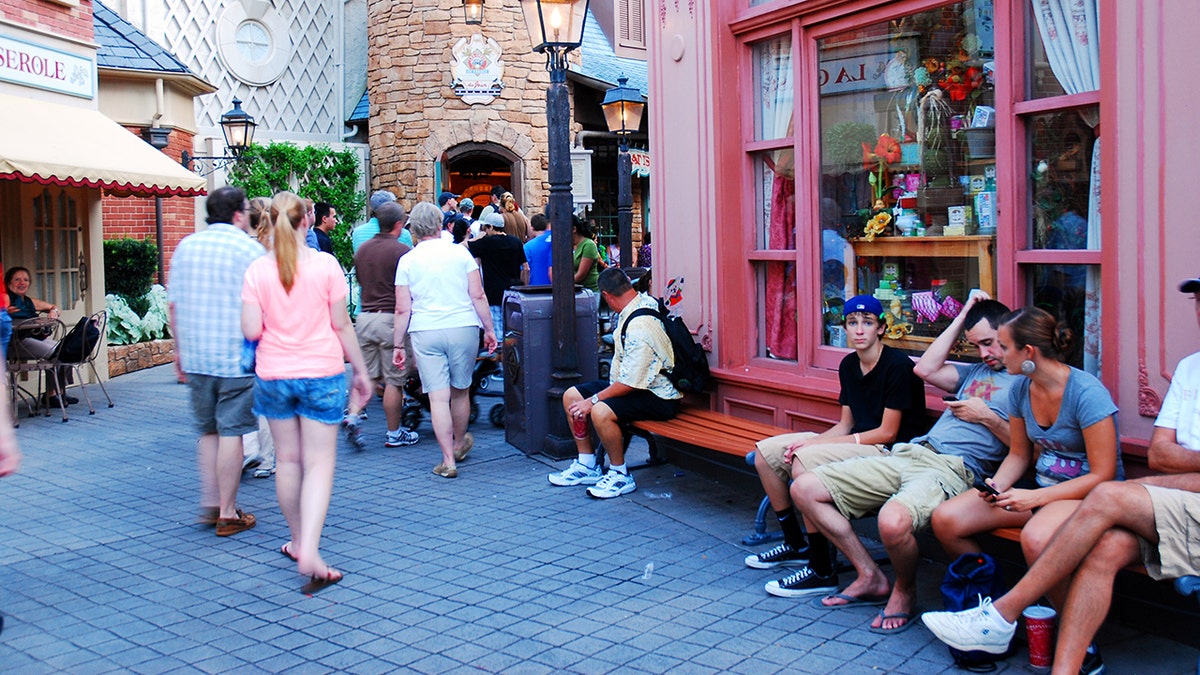 Adultos sentados do lado de fora das lojas com temas franceses no Walt Disney World Park