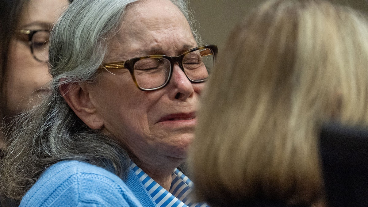 Donna Adelson wearing blue sweater and glasses as she cries in court