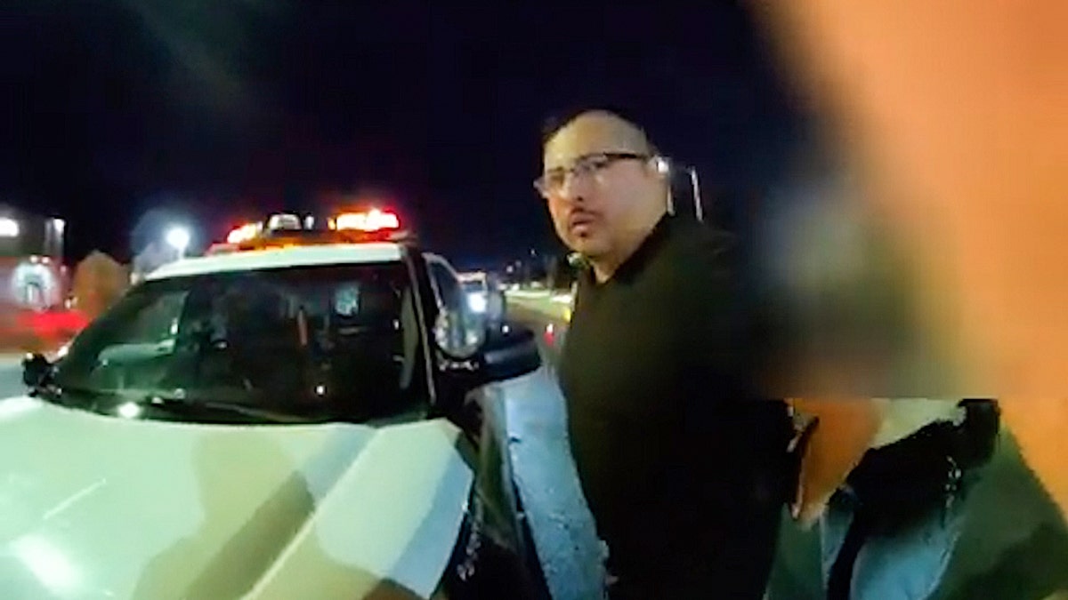 Man in glasses standing near police car at night.