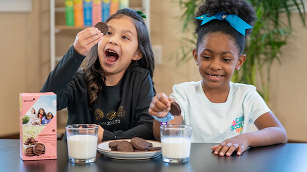 Two young girls enjoy research, new girl scout cookies, on a plate with milk.