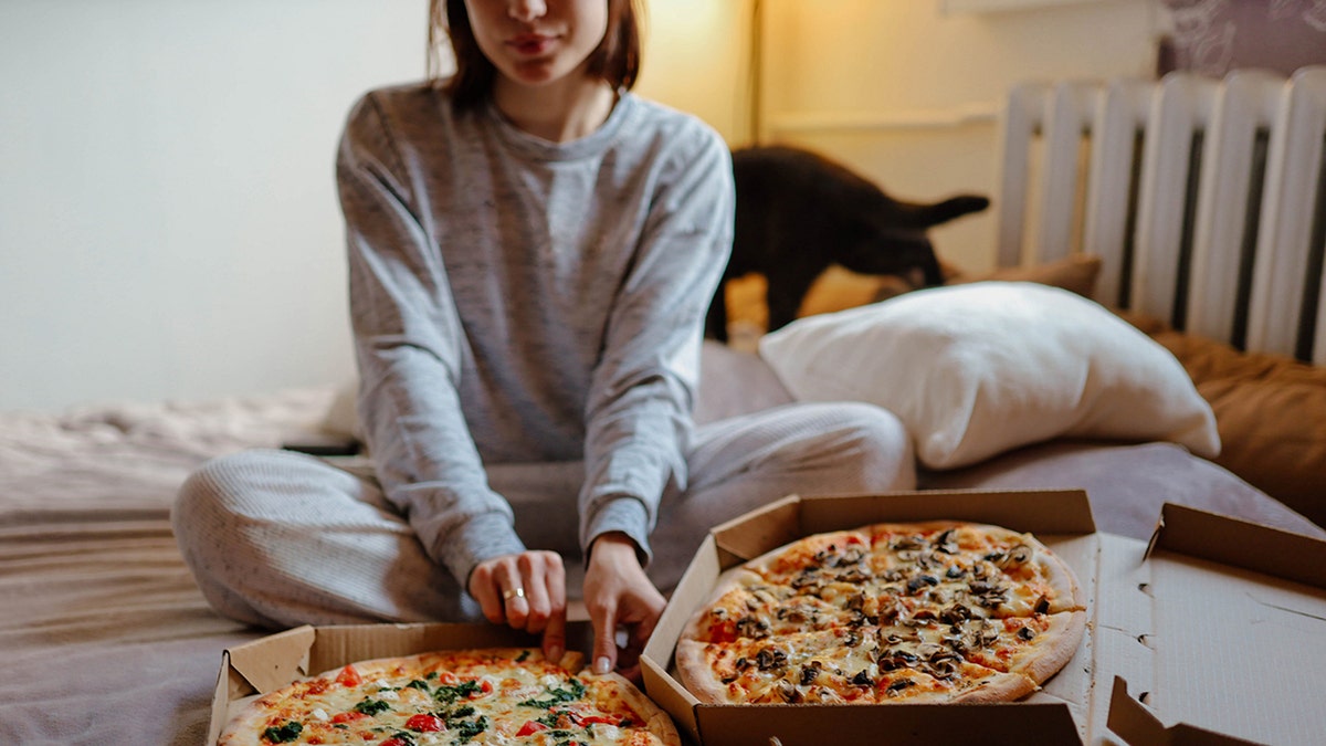 woman eating pizza on bed