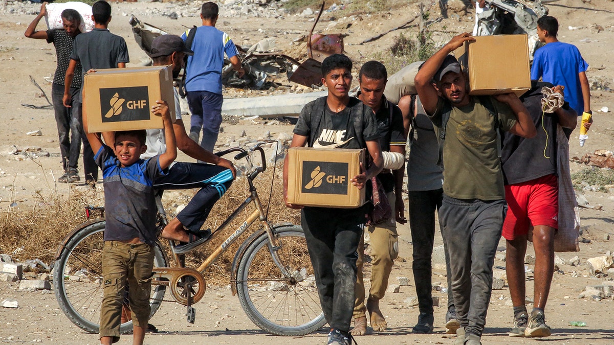 Gazans walk with humanitarian aid boxes they have received in a distribution center led by the United States and Gaza Humanitarian Foundation (GHF), supported by the United States.