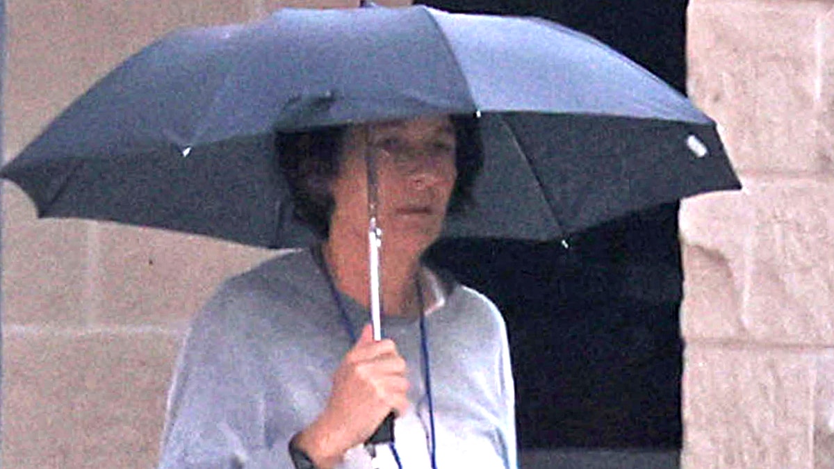 Ghislaine Maxwell in gray prison sweats carrying an umbrella as she walks through a prison yard