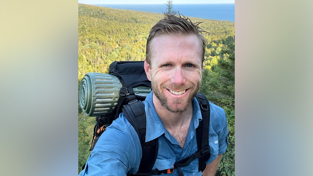 Grant Gardner smiling and posing for a photo in a field while hiking