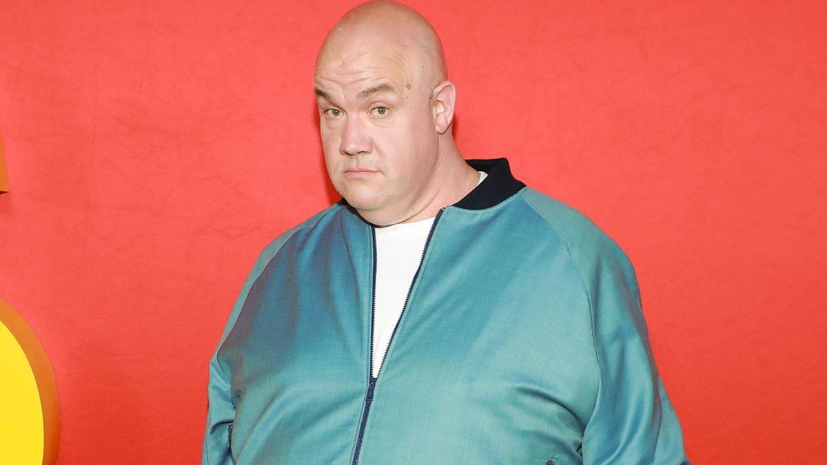 Guy Branum looks at the camera while posing on the red carpet.