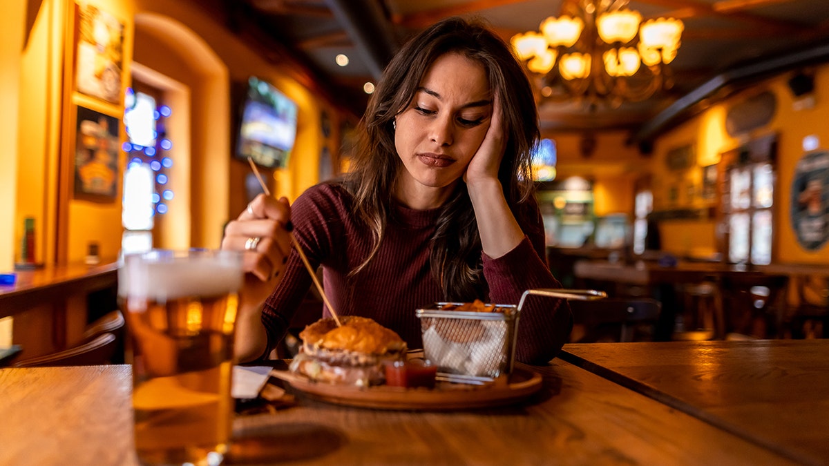 Forlorn woman eating burger with beer at bar