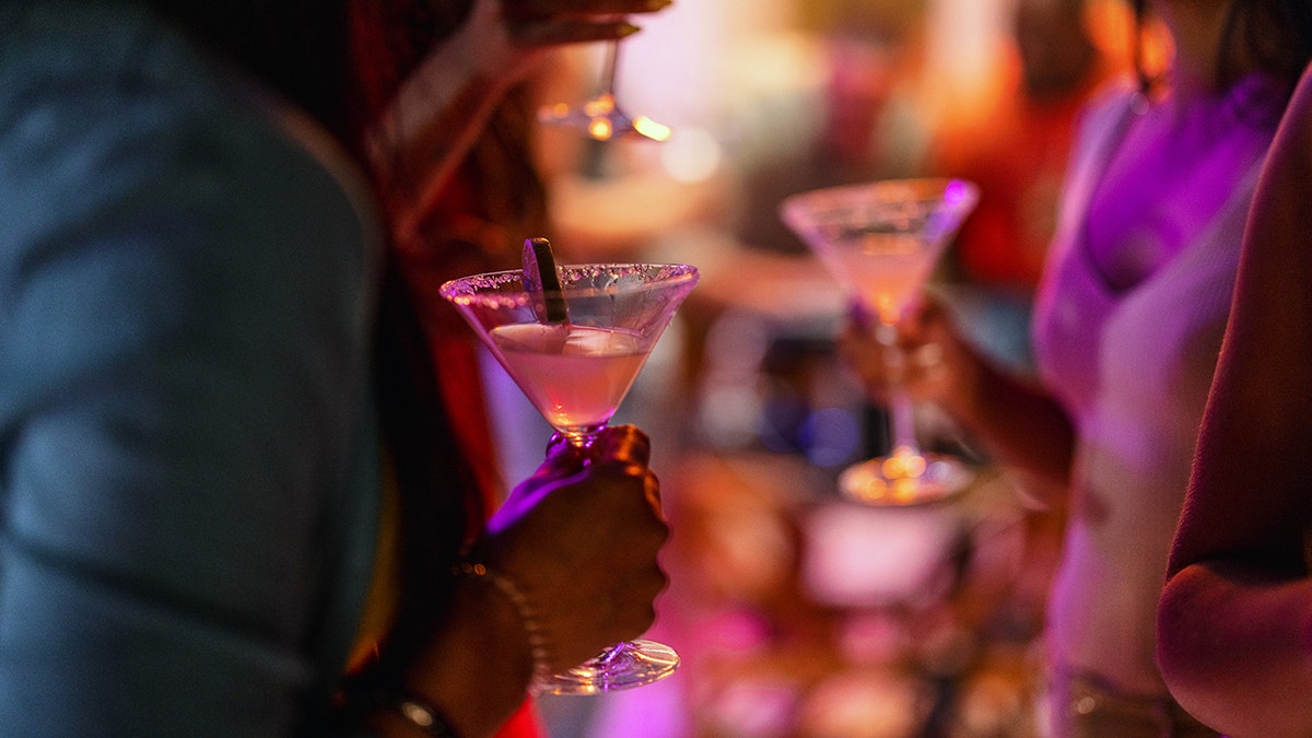 Woman holding cocktail speaking to other bar patrons