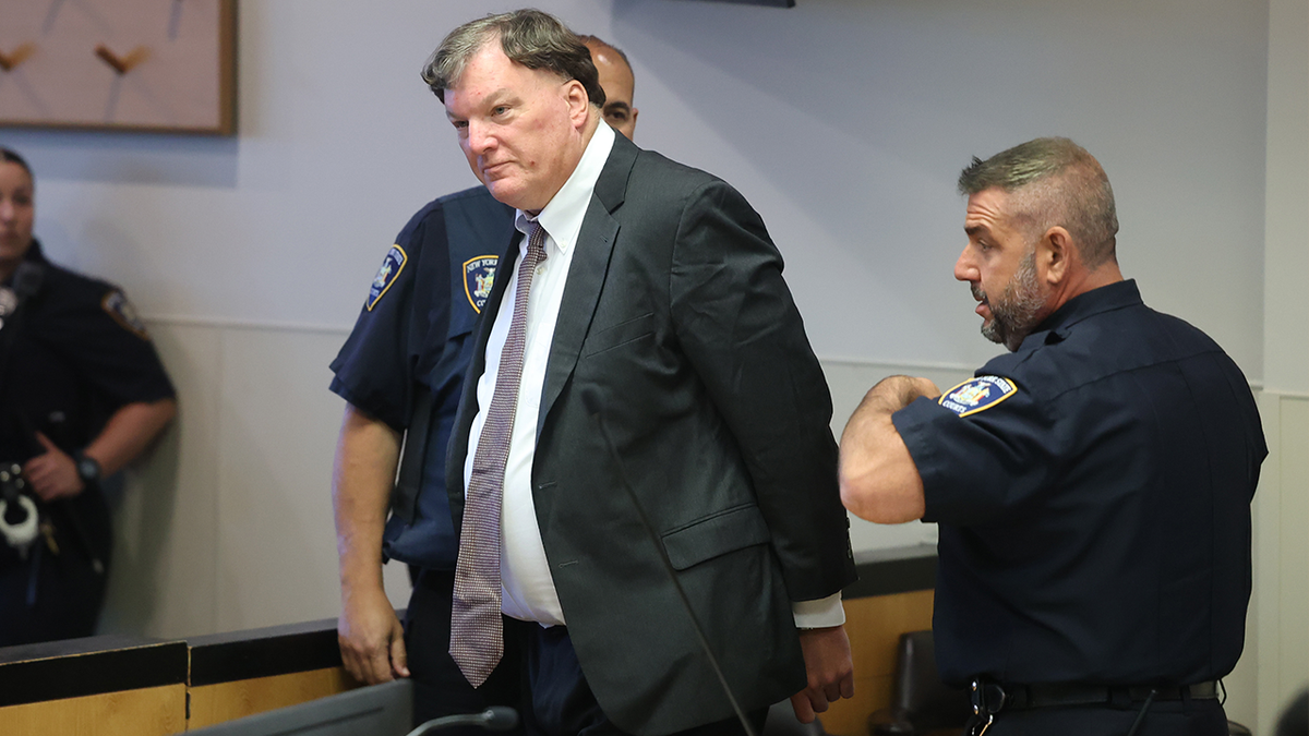 Rex Heuermann wearing a suit in court as two officers stand at his sides.