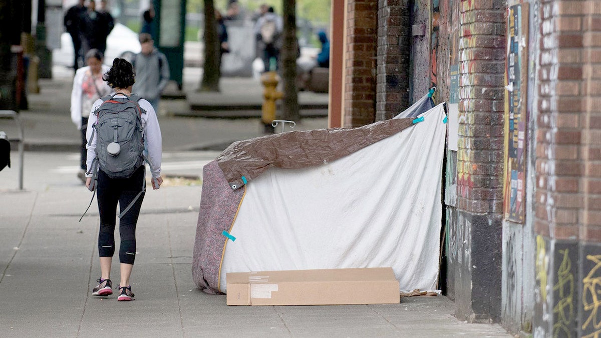 A pedestrian walking past a makeshift tent encampment on a street in Seattle's Pioneer Square neighborhood