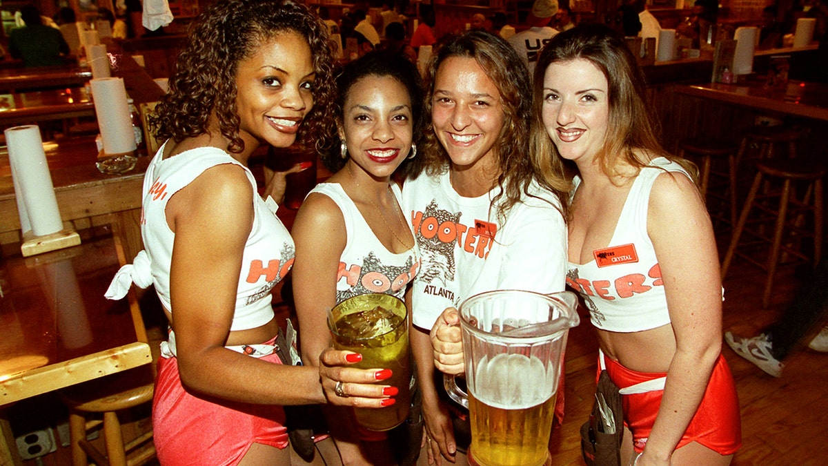 Four beetrogen couple smiling on camera while holding drinks.