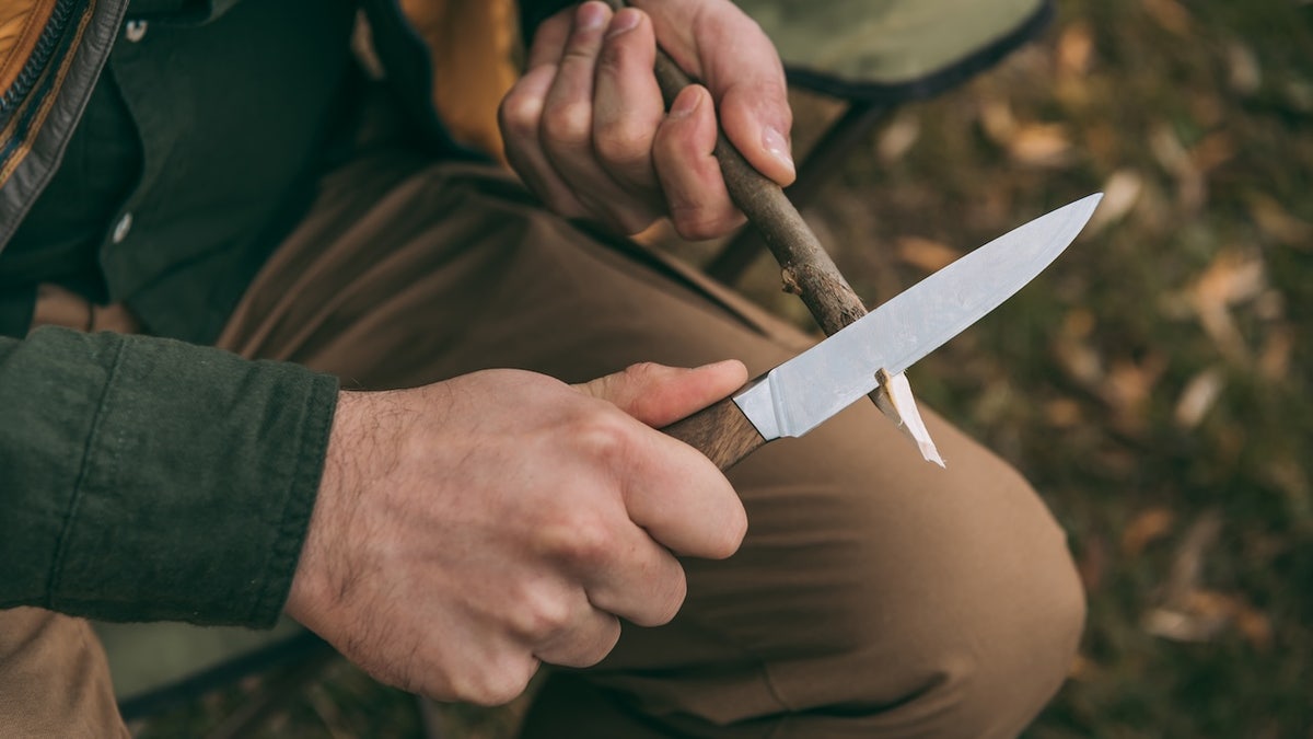 man sharpening branch with knife