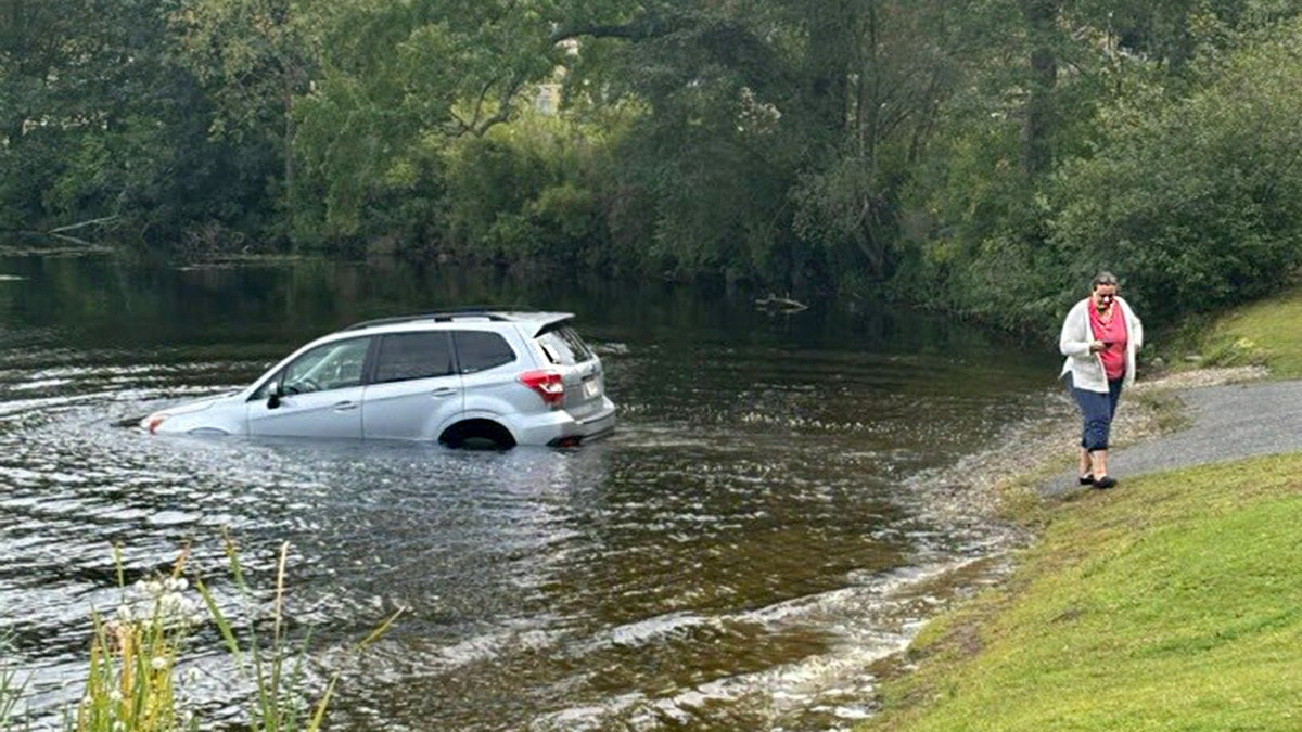 A woman stands on shore as her car sinks in the lake