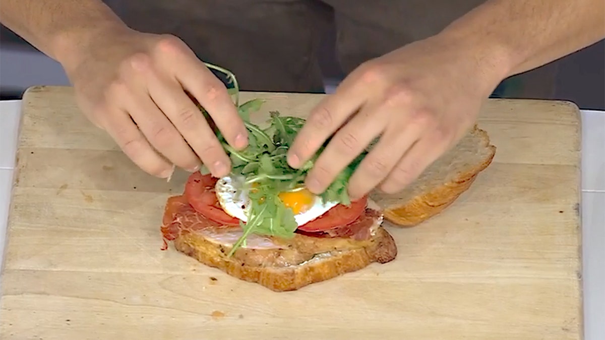 Han, yumurta, prosciutto ve roka içeren yemek kitabından kahvaltı kulübü sandviç yapıyor.