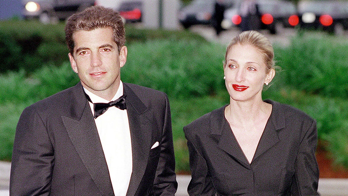 JFK Jr. and Carolyn Bessette-Kennedy walking together in matching black attire outdoors.