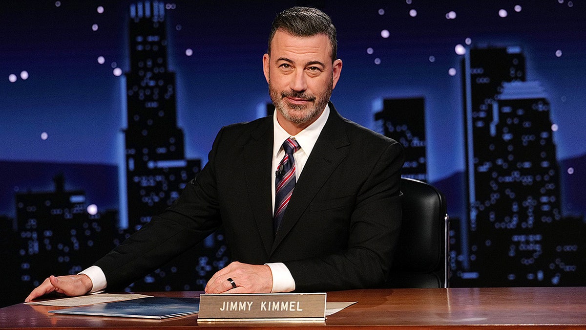 Comedian Jimmy Kimmel sits at the desk on his set