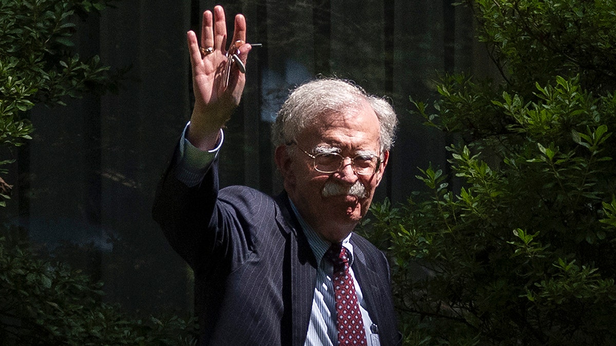 John Bolton waves outside his home in suit