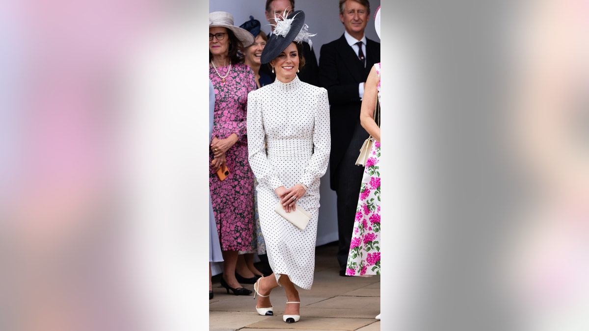 Kate Middleton does a curtsy in a white and black polka dot dress.
