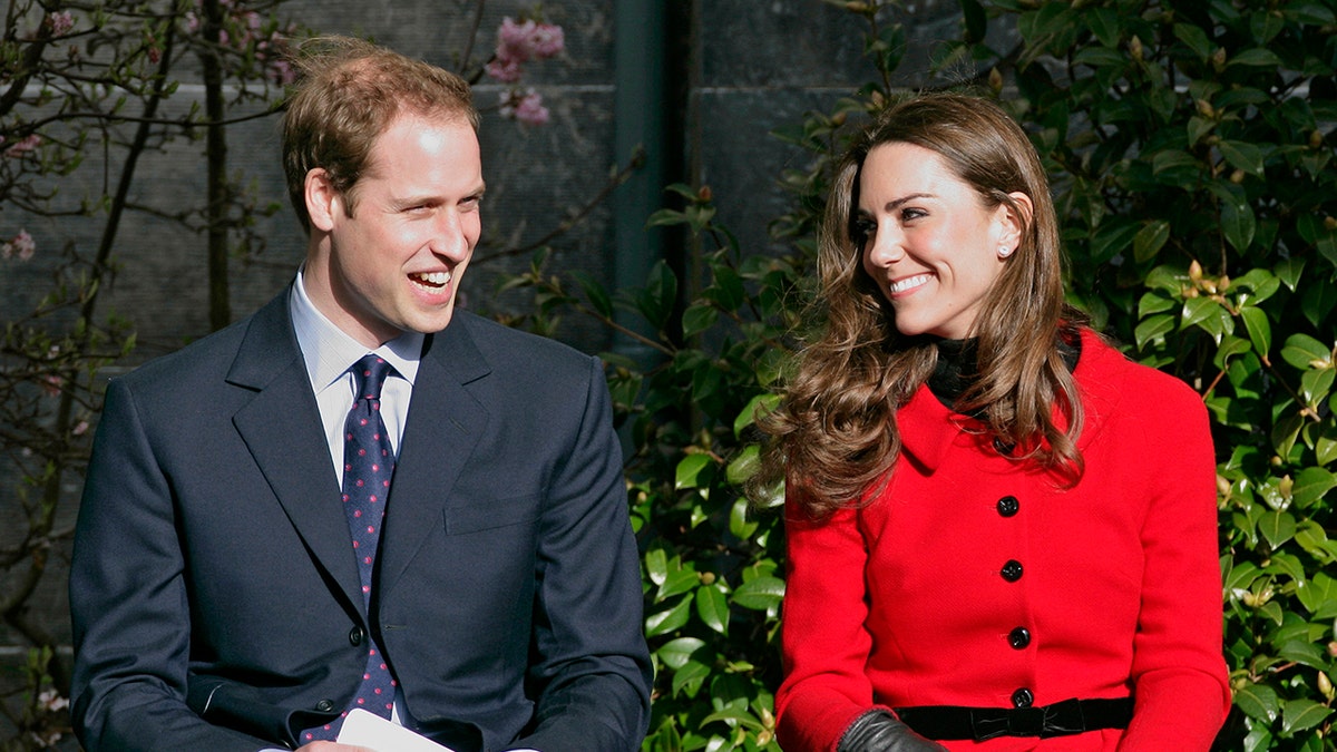 Prince William and Kate Middleton smiling at each other in formal wear outside the University of St. Andrews.