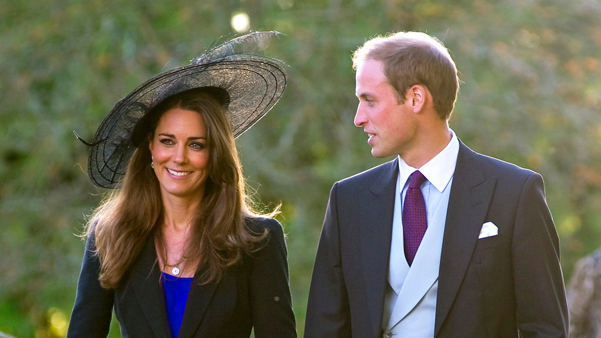 Prince William and Kate Middleton in formal wear walking together and smiling as they head to a wedding.