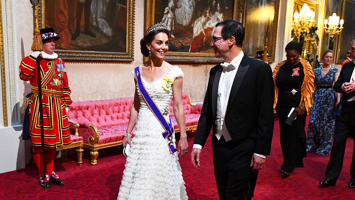 Kate Middleton wearing a white gown speaking to a well dressed man during a state banquet.