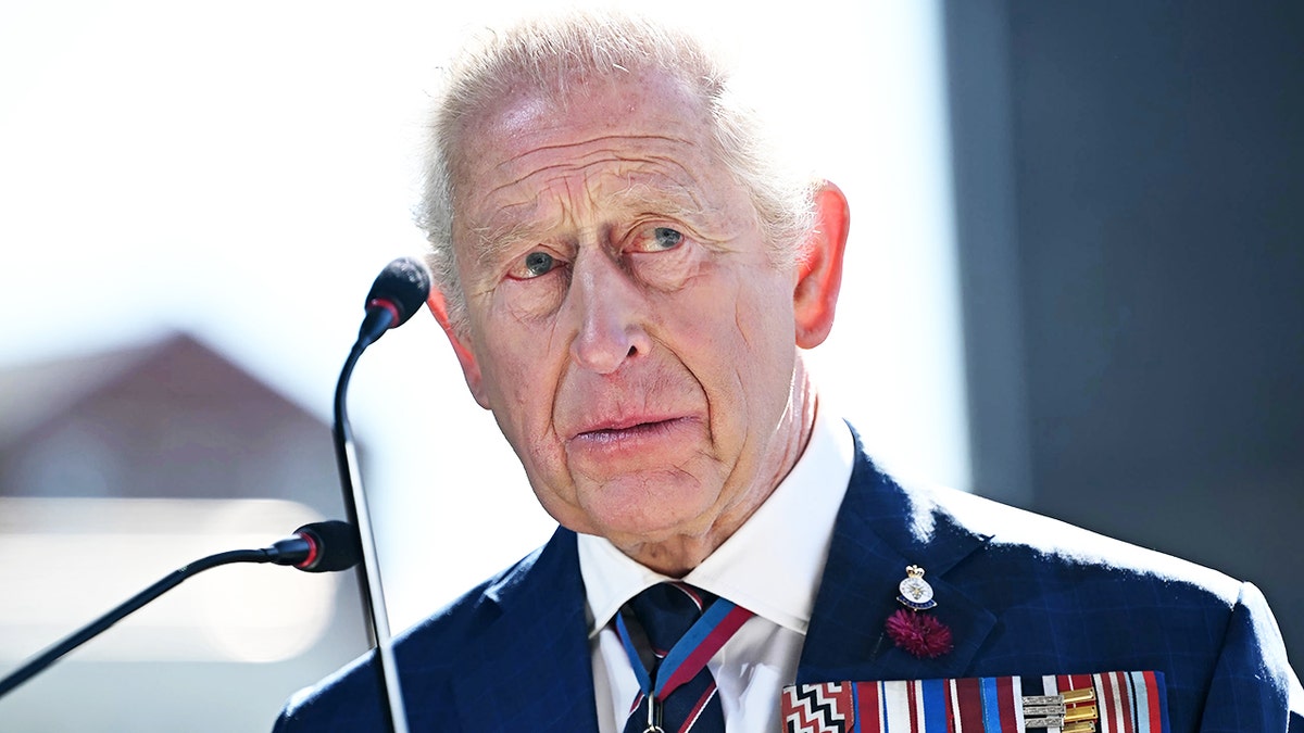 A close-up of King Charles looking serious in a suit with medals.