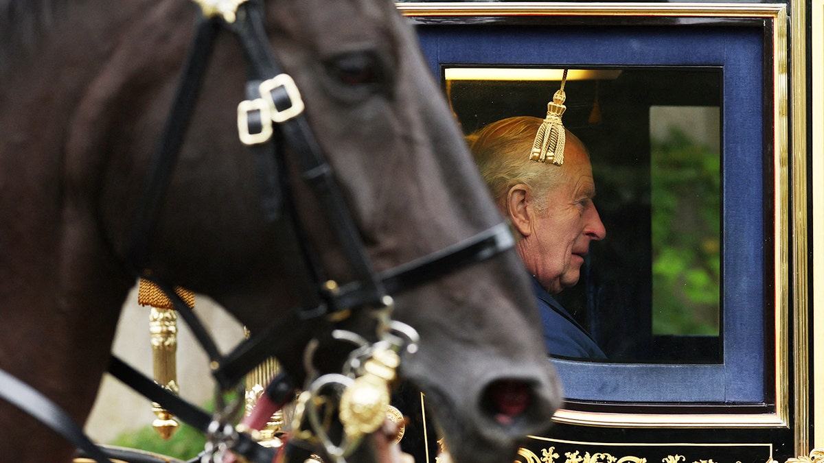 King Charles inside a royal carriage next to a horse.