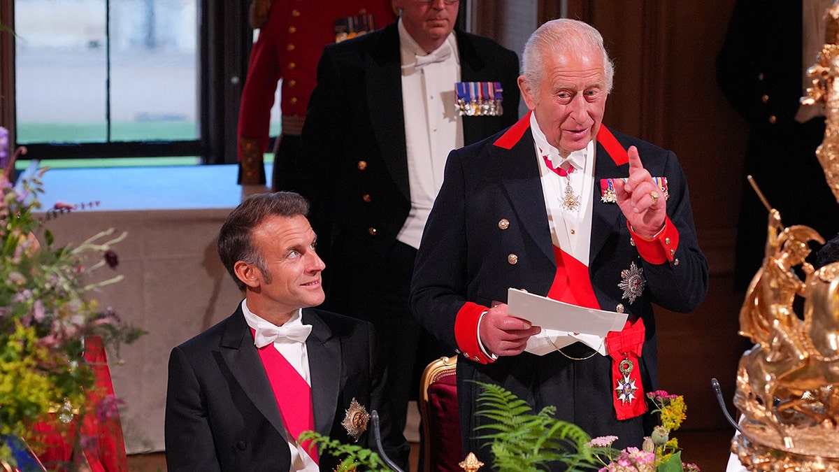 King Charles giving a speech as President Macron sitting at a table looks on.