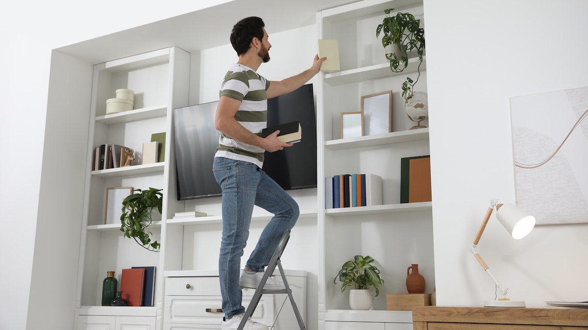 Man on metal folding ladder taking book from shelf 