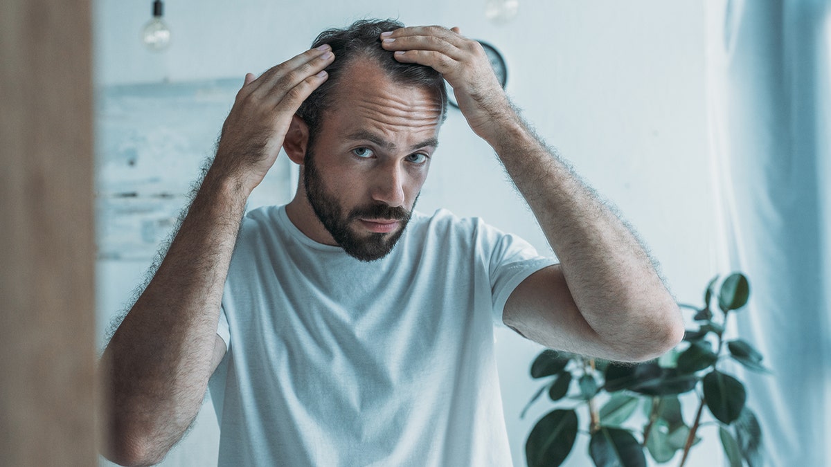 Man looking at himself in the mirror, inspecting hair loss, evident through receding hairline