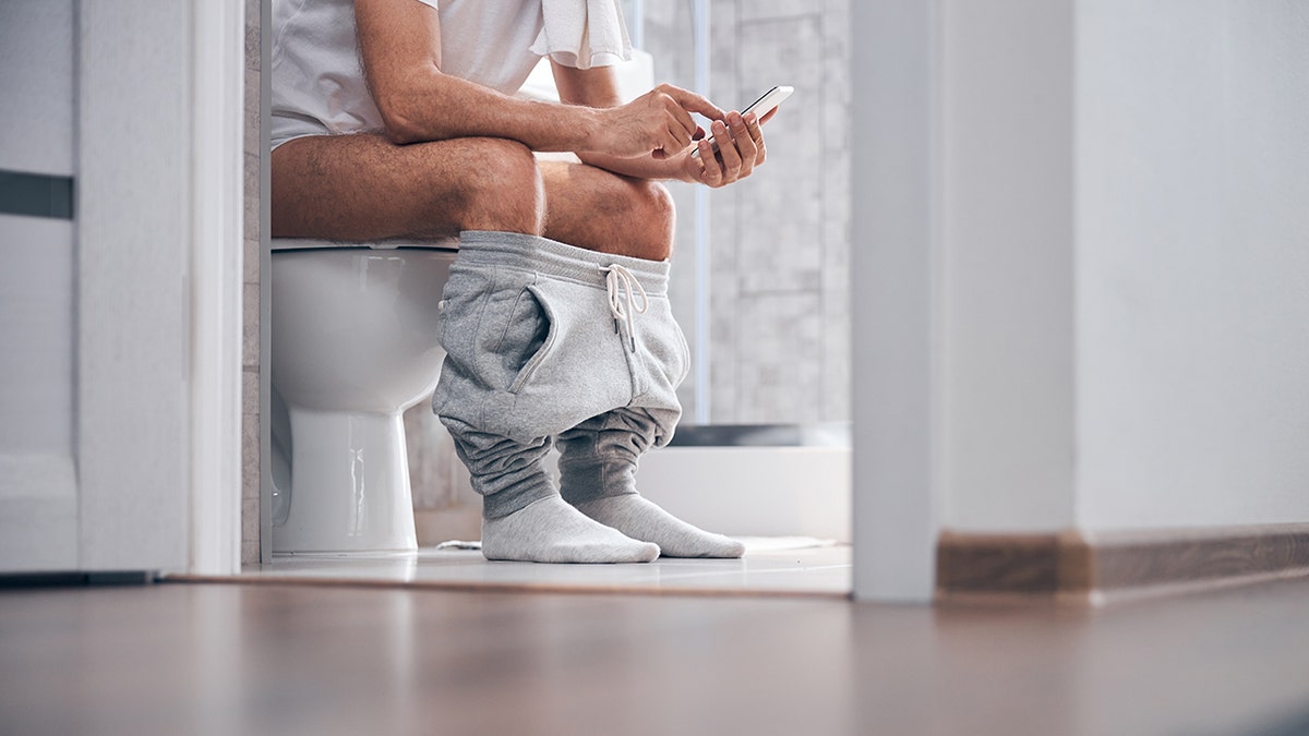 Man sitting on toilet while scrolling on smartphone