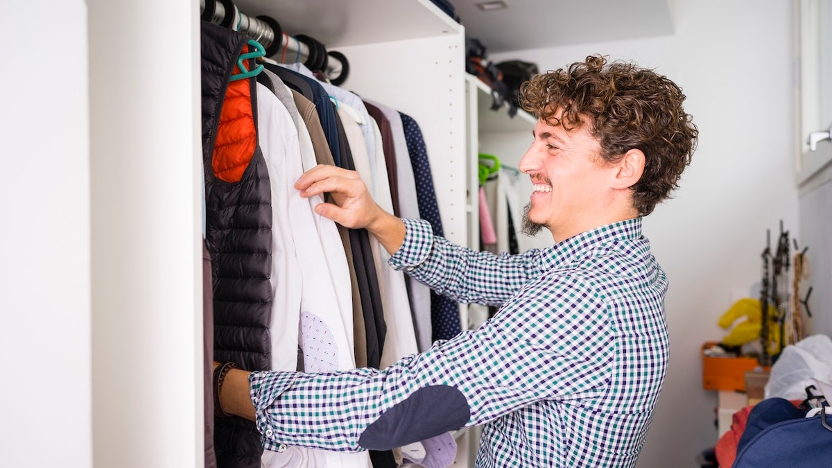 Young man looking for shirts in wardrobe