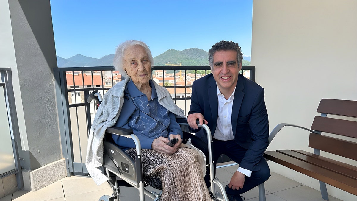 Maria Branyas in a wheelchair outside posed next to a man