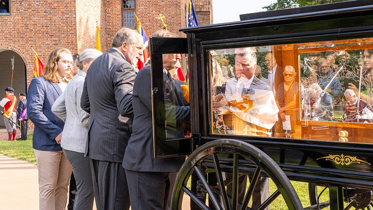 Men lifting coffin out of black hearse wagon