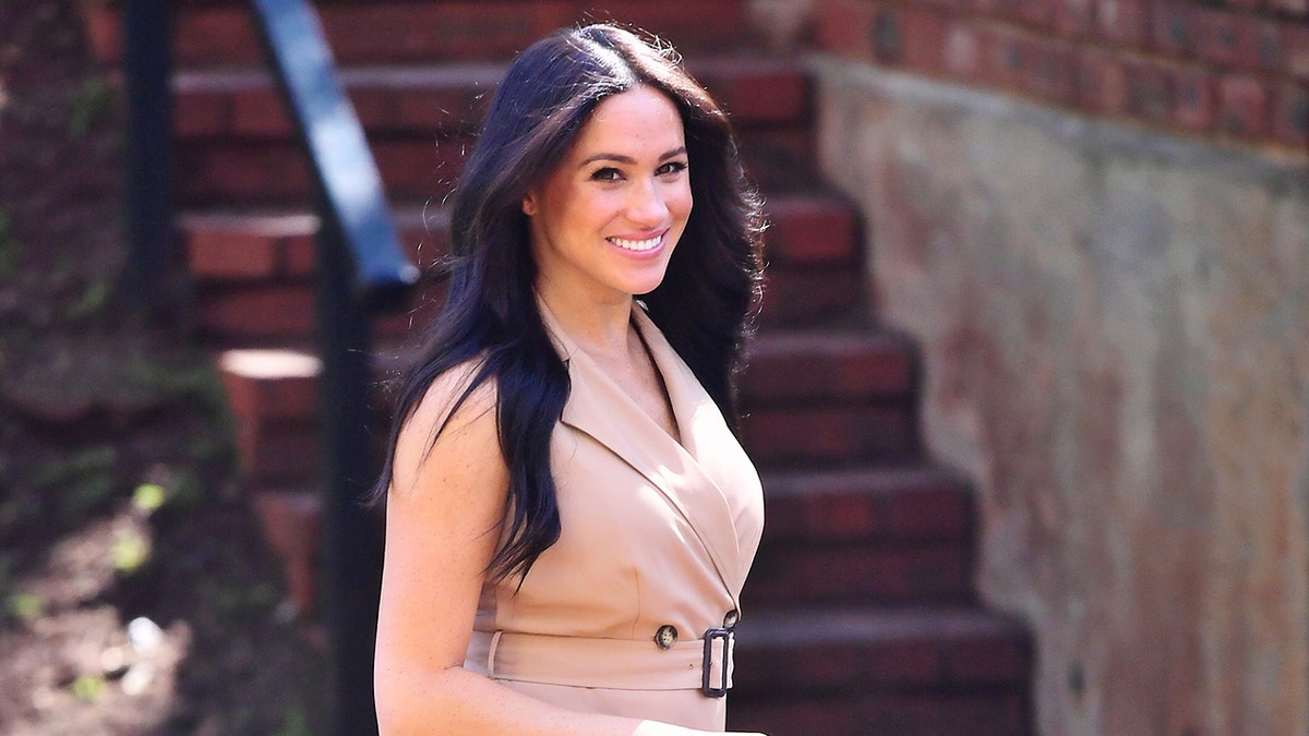 Meghan Markle smiling wearing all beige walking outdoors.