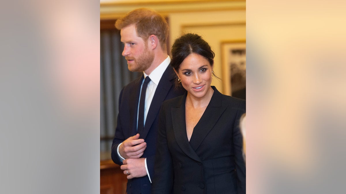 Meghan Markle speaking to someone as Prince Harry looks on.
