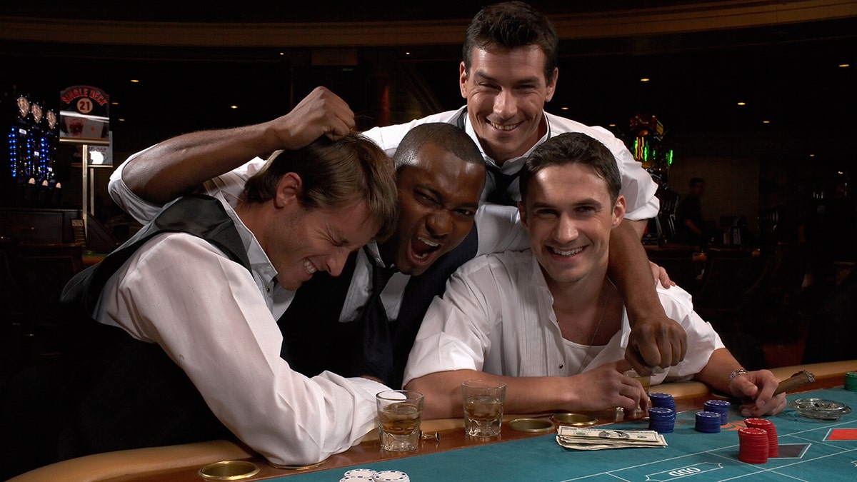 Group of men sitting in Vegas casino, clowning around with money, drinks and chips in front of them.