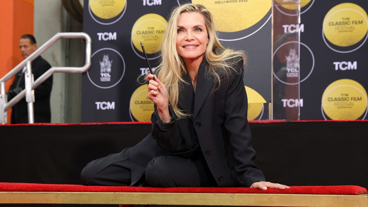 Michelle Pfeiffer sits on a stage at her hand and footprint ceremony