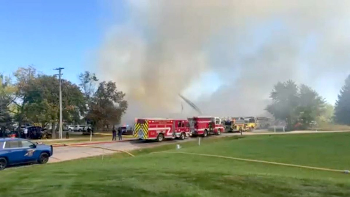 law enforcement and fire officials parked on street as smoke billows into air