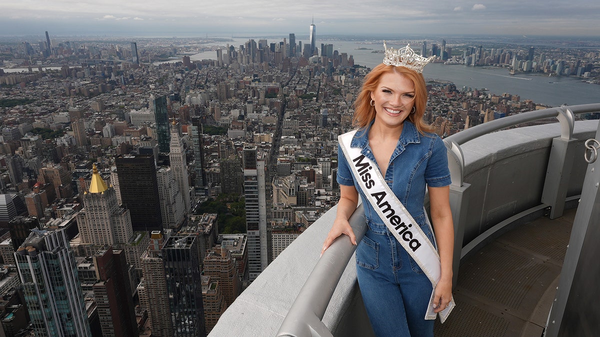 Miss America wearing a denim jumpsuit with a sash overlooking New York City.