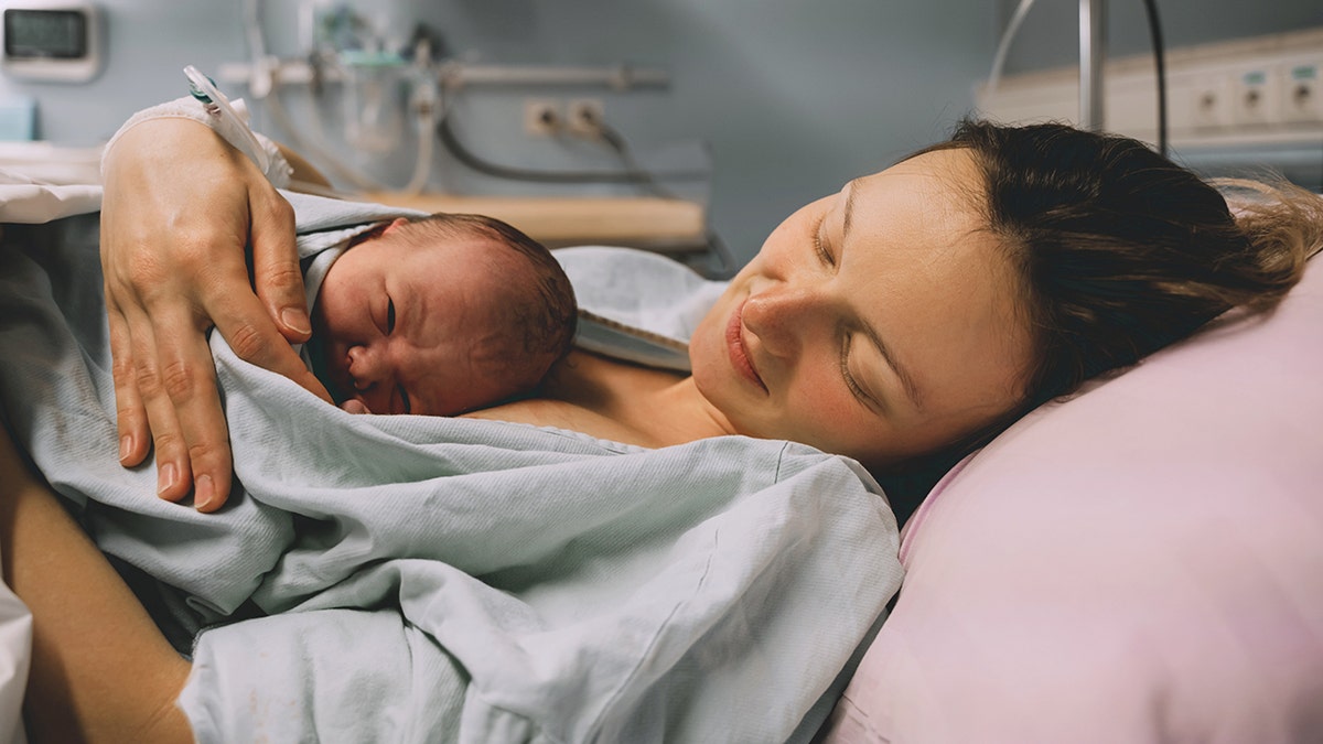 Woman laying in hospital bed looking down smiling at newborn on her chest.