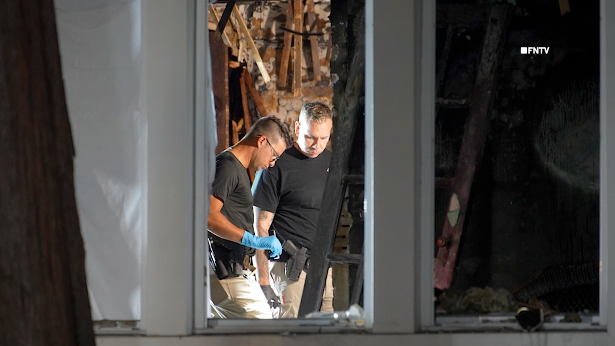 FDNY fire marshals investigating the crime scene, pictured through a broken, burned window